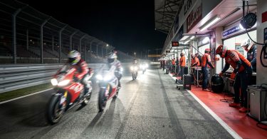 Motos de course d'endurance de nuit sur le circuit du Mans avec mécaniciens dans les stands illuminés