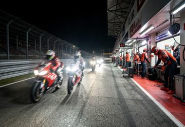 Motos de course d'endurance de nuit sur le circuit du Mans avec mécaniciens dans les stands illuminés